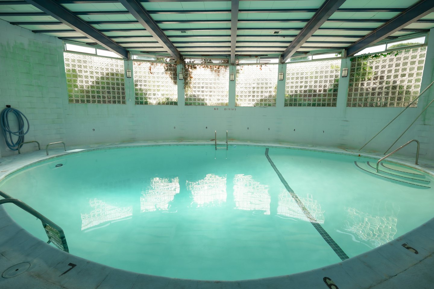Piscina interior vacía con agua clara y escaleras metálicas.