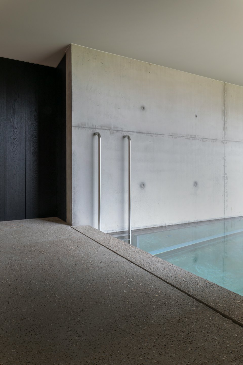 Moderna piscina interior con escaleras de acero inoxidable junto a paredes de hormigón.