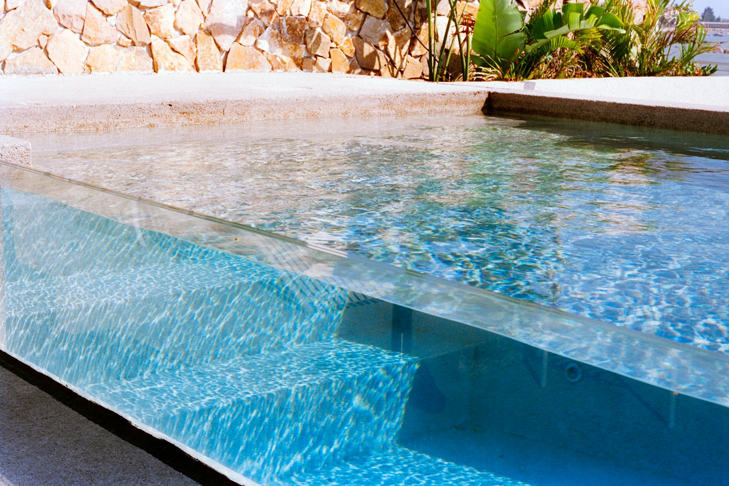 Piscina moderna con bordes de cristal y azulejos de mosaico azul.