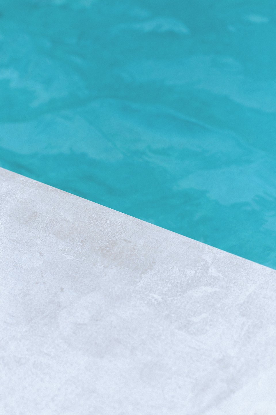 Borde de piscina con remate de hormigón y agua turquesa.