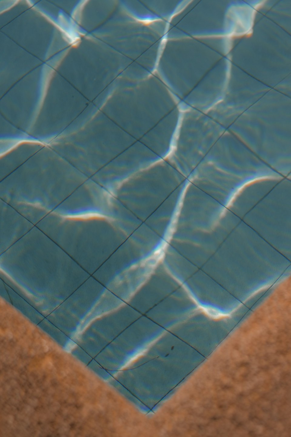El sol se refleja en las baldosas azules de una piscina.