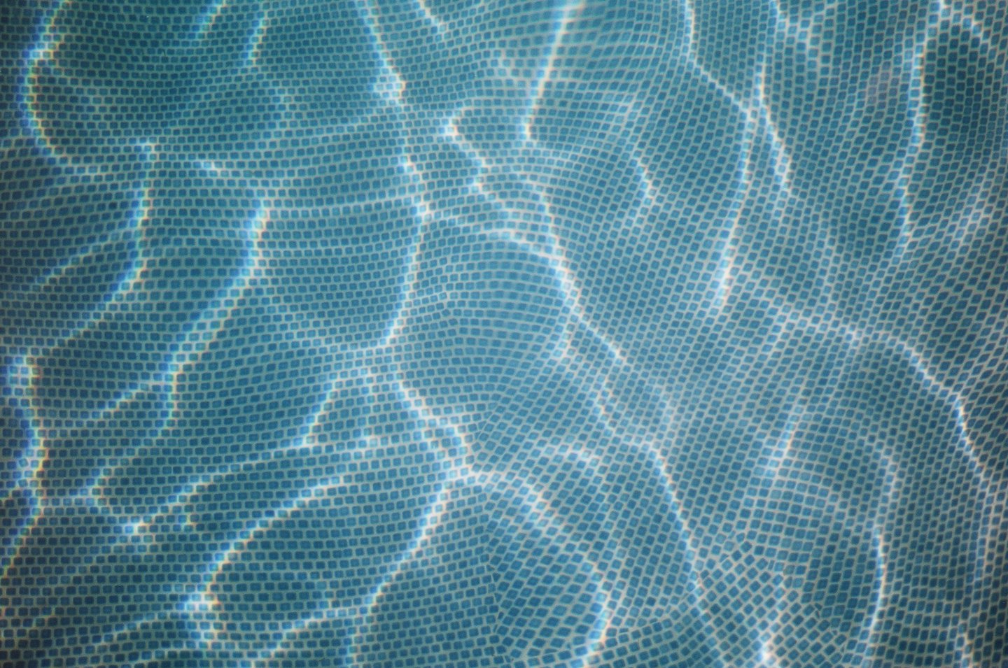Patrones de luz solar brillan sobre azulejos de mosaico azul bajo el agua.
