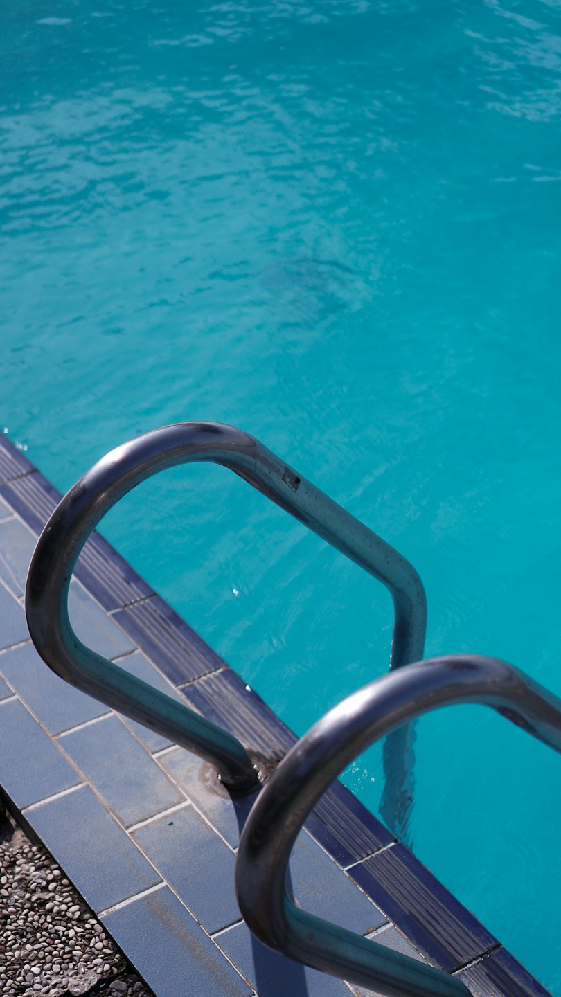 Escalera de piscina de metal sumergida en agua clara y ondulada.