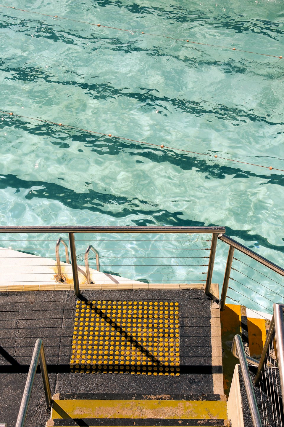 Barandillas de acero inoxidable conducen a una piscina de color turquesa transparente.