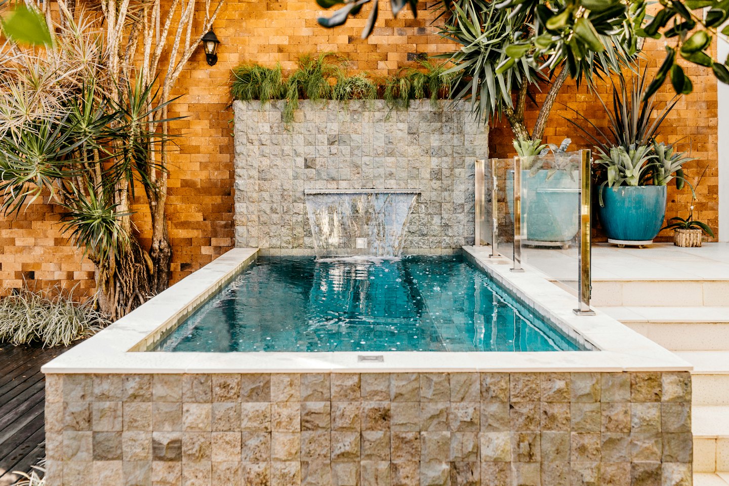 Cascada de piedra que desemboca en una piscina moderna con plantas.